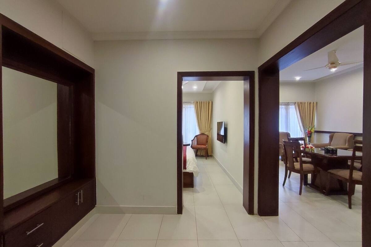 A hotel room with a large bed, a TV, and a dining area with chairs and a table.