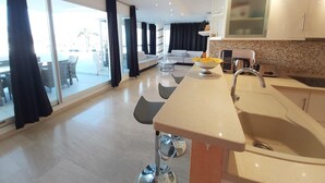 A modern kitchen with a large island, a dining area with a white sofa, and a view through large sliding doors to an outdoor patio.