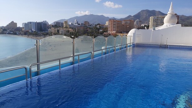 A swimming pool with a view of a beach and mountains in the background.
