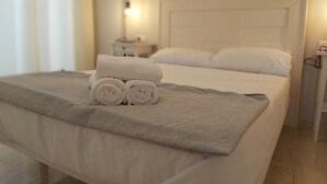 A neatly made bed with white linens and a grey blanket, a bedside table with a lamp, and a wall clock.