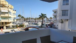 A balcony with wicker furniture, overlooking a marina with boats and palm trees.