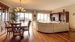 A spacious living area with a dining table, chairs, a sofa, and a large window offering a view of the city. - Monumental Ocean View by Atlantic Holiday (Funchal)