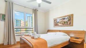 A hotel room with a wooden bed, a nightstand, a painting on the wall, and a window with a view of buildings. - Monumental Ocean View by Atlantic Holiday (Funchal)