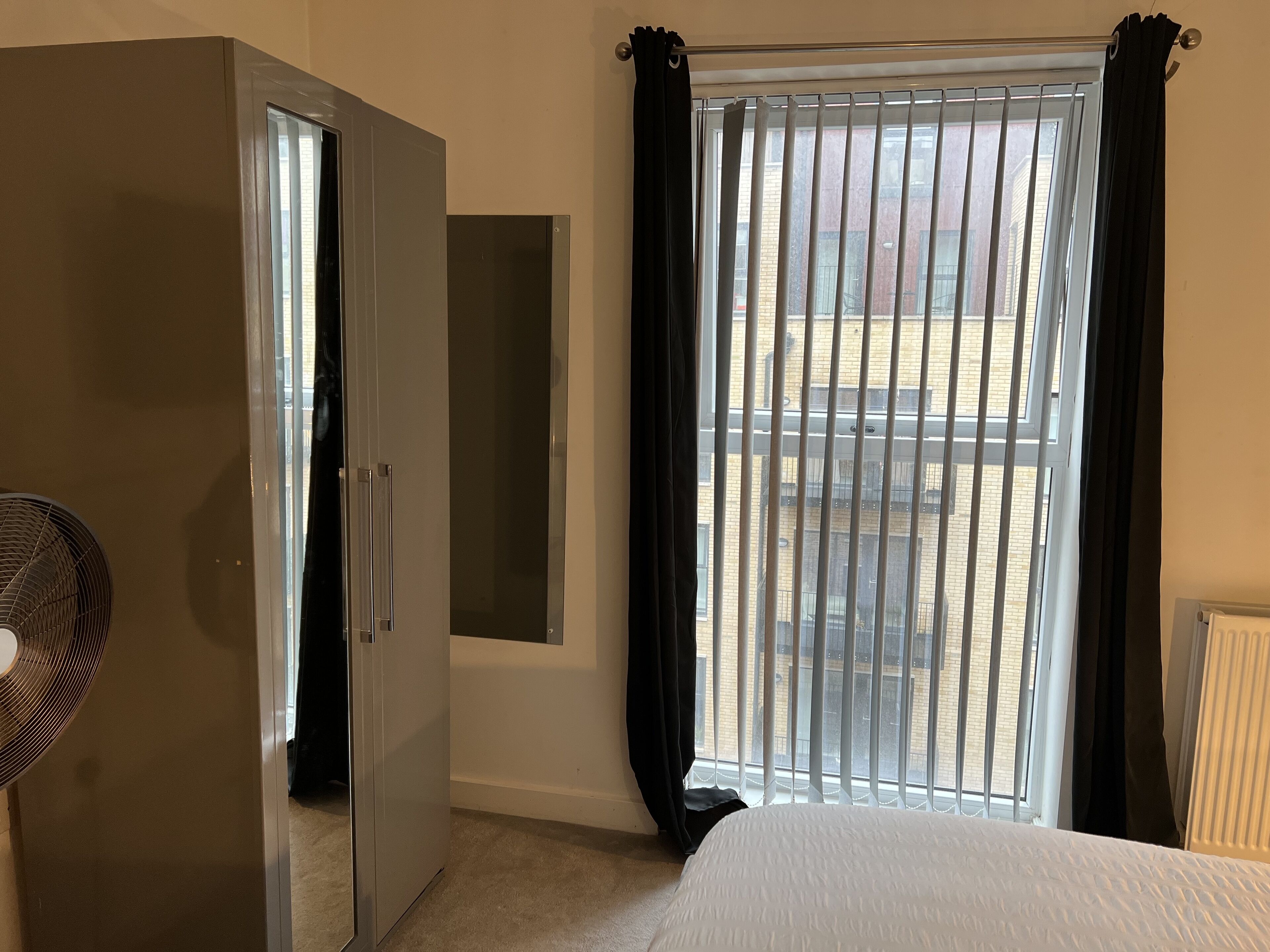 A bedroom with a bed, a wardrobe, a radiator, and a window with blinds.