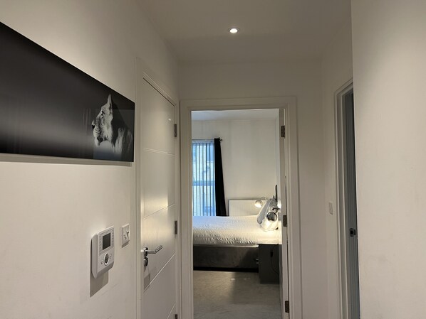 Ein Flur, der in ein Schlafzimmer mit einem Bett, einem Nachttisch und einer wandmontierten Steuerungsmöglichkeit führt.