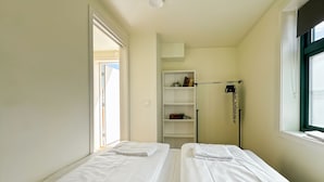 A room with two beds, a wardrobe, a shelf with books, and a window.