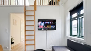 A modern living room with a TV mounted on the wall, a wooden ladder, a sofa, and a window with a view.