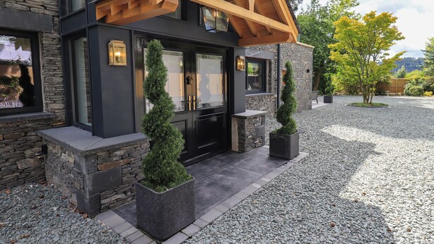 A modern house with a stone facade, wooden beams, and a gravel driveway. - Hare's Breath (Windermere)