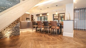 A modern kitchen with a stone accent wall, wooden staircase, and a dining area with leather chairs. - Hare's Breath (Windermere)