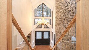 A modern interior with a wooden staircase, a stone wall, and a chandelier. - Hare's Breath (Windermere)