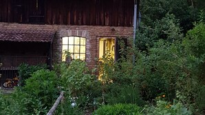 A rustic wooden building with a tiled roof, surrounded by dense greenery and a garden area.