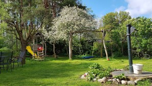 A garden with a wooden playhouse, a swing set, and a hose reel.