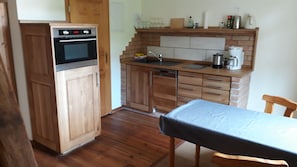 Una cocina compacta con armarios de madera, horno empotrado, lavamanos y una mesa de comedor con mantel.