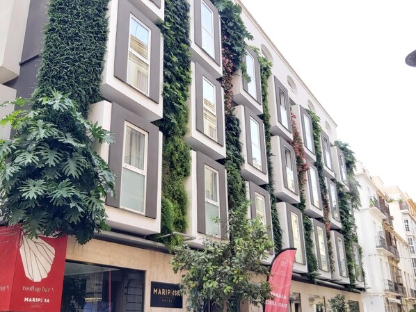A hotel facade with multiple windows, some covered with greenery, and a visible sign for 'Mariposa Hotel'.