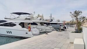 Un port de plaisance où sont amarrés plusieurs yachts, une promenade pavée et une petite construction surmontée d’un drapeau.