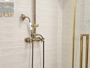 Een douche met een messing fitting, witte betegelde wanden en een bordje met de tekst 'PARQUE LATS'.