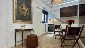 Una habitación con piso de espiga, una mesa de comedor con sillas, un sofá, una pequeña mesa redonda con una lámpara y un cuadro en la pared.
