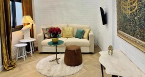 Un salon avec un mur en briques blanches, un canapé beige, une petite table ronde avec un vase et une lampe.