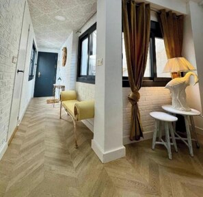 Un couloir avec un parquet en chevrons, un canapé jaune, une lampe blanche et une sculpture d’oiseau blanc posée sur un tabouret.