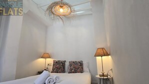 Una habitación de hotel con una cama, dos lámparas, una mesita y un candelabro en el techo.