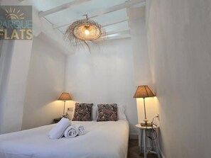 Une chambre d’hôtel avec un lit, deux lampes, une petite table et un luminaire au plafond.