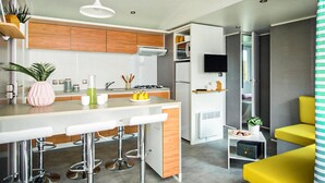 Una cocina moderna con una isla central, taburetes de bar, microondas y un televisor montado en la pared.