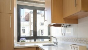 A modern kitchen with wooden cabinets, a stainless steel sink, and a window with a view of buildings. - Del Parque Flats Cervantes: Cozy Apartment for 4 in Historic Málaga Center (Málaga)