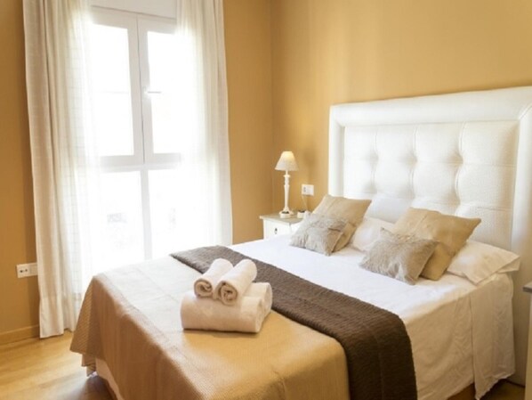 Una habitación de hotel con una cama grande, una mesita de noche con una lámpara y una ventana con cortinas.