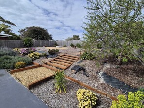 A garden with raised beds, a wooden deck, and various plants. - Beach Retreat House with Fire Pit near Hot Springs (Capel Sound)