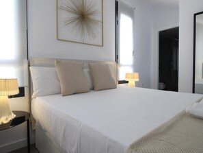 A neatly made bed with two pillows, a bedside table with a lamp, and a wall art piece above the bed.