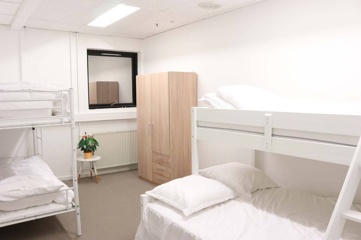 Une chambre de dortoir avec des lits superposés, une armoire en bois, une petite table avec une plante et une fenêtre avec un miroir.