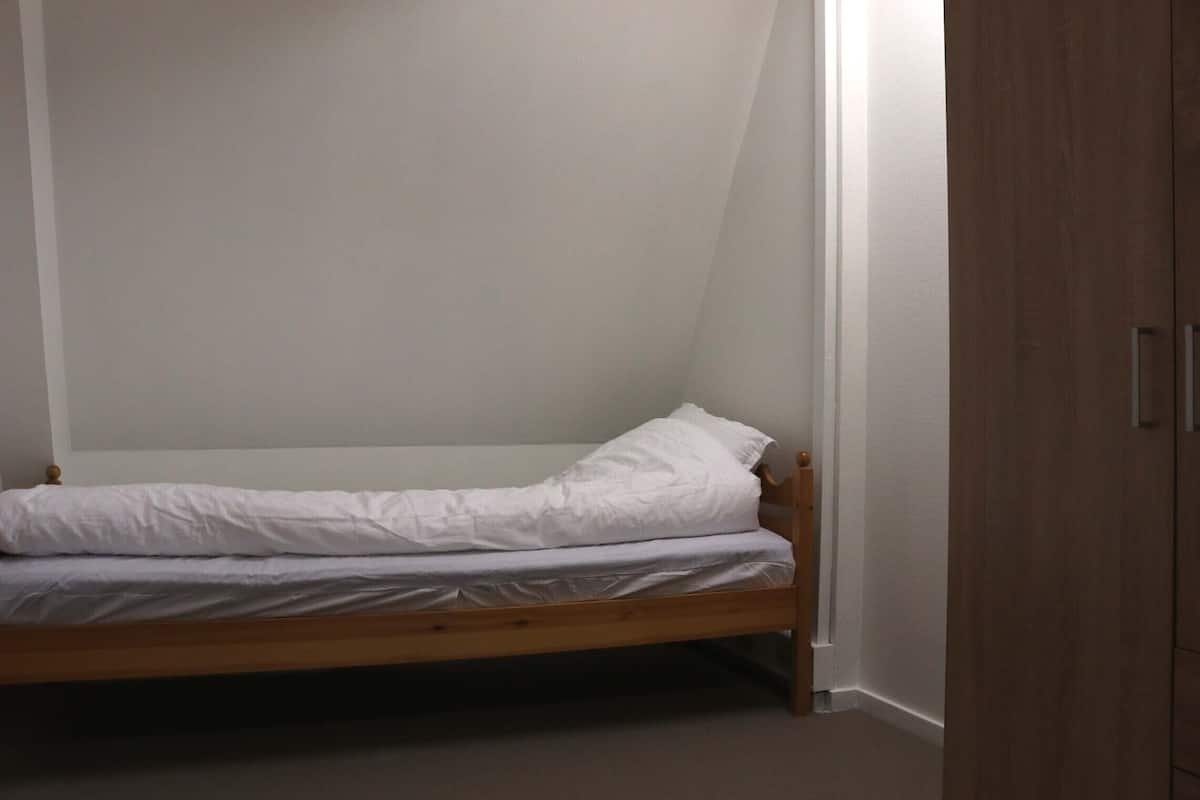 Une petite chambre avec un lit simple, un cadre en bois et du linge de lit blanc.