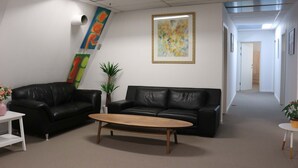 A modern office space with two black leather sofas, a wooden coffee table, and a white desk with a pink vase.