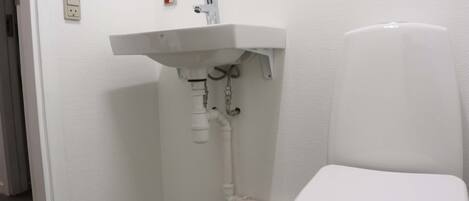 Un baño con lavamanos blanco, inodoro y fontanería visible.