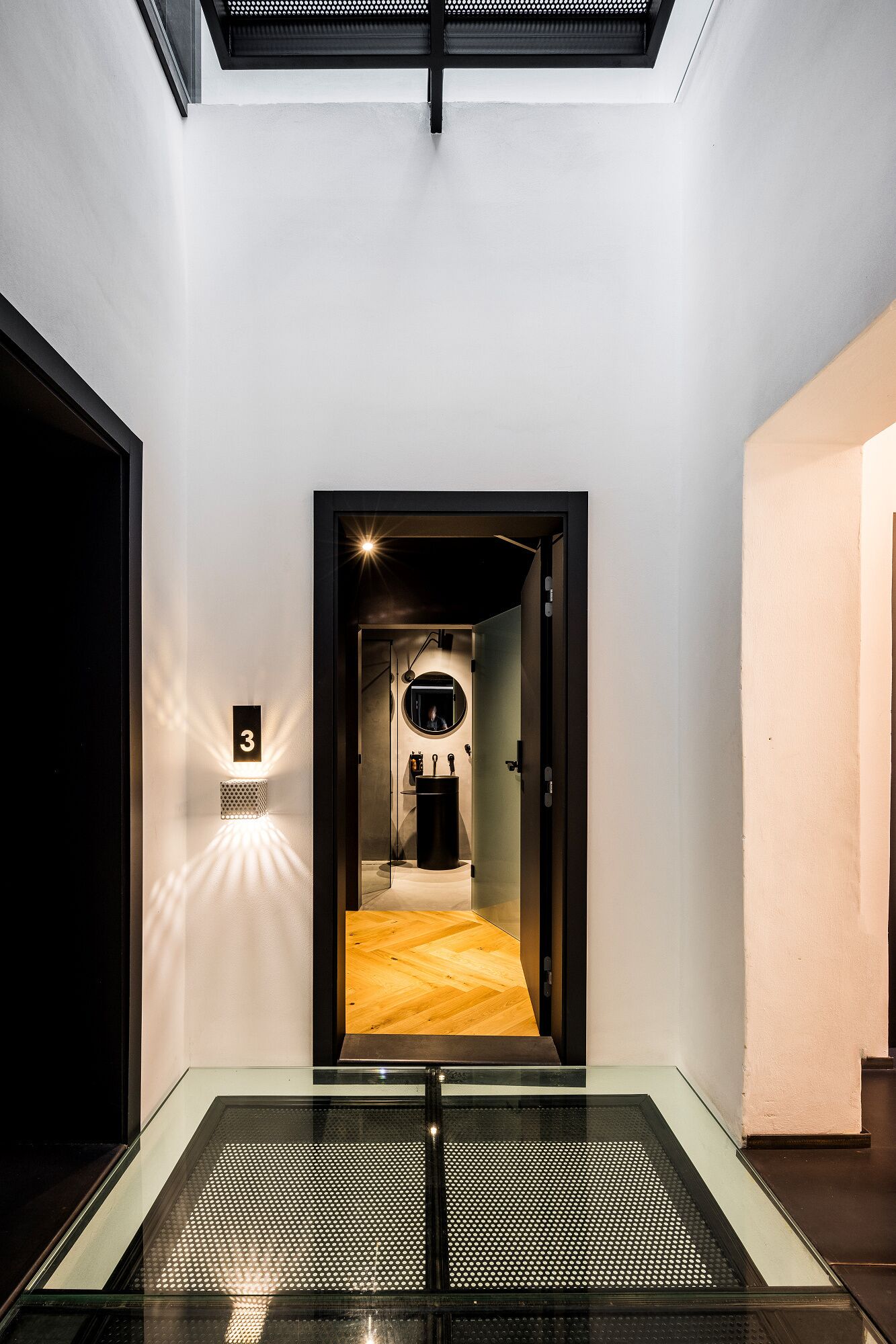 Een modern interieur met een glazen lift, een gang die leidt naar een kamer met een houten vloer, en een nummerbord '3' aan de muur.