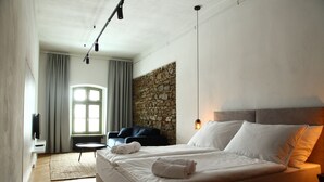Ein modernes Hotelzimmer mit einem großen Bett, einer Wand mit Steinverkleidung, einer Sitzecke mit kleinem Tisch und einem großen Fenster mit Vorhängen.