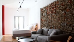 Ein modernes Wohnzimmer mit einem grauen Sofa, einem runden Couchtisch und einem Korbstuhl. Eine Steinwand verleiht dem Raum Struktur.