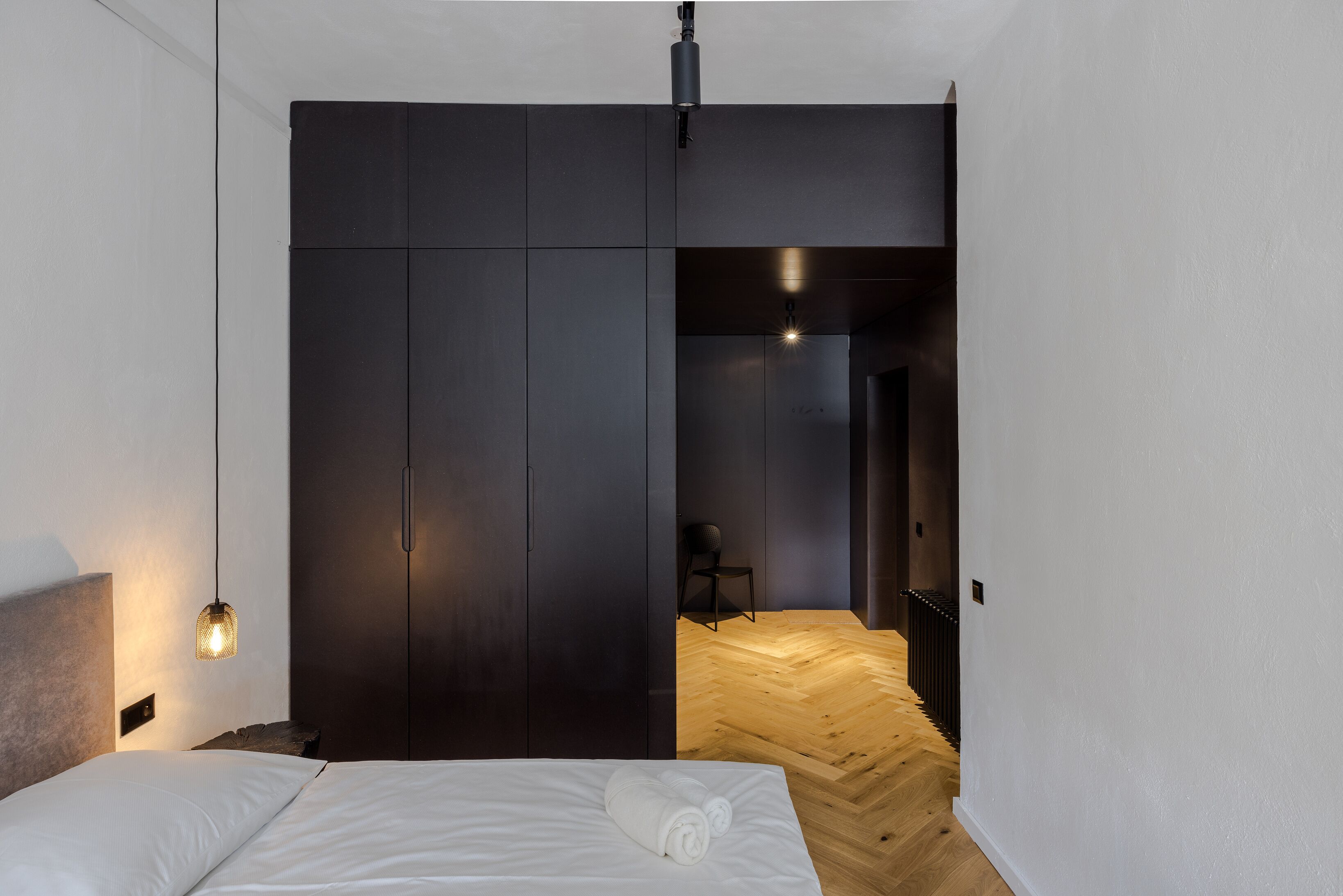 A modern bedroom with a large wardrobe, a neatly made bed, and a wooden floor.