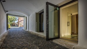 Un pasillo adoquinado que conduce a un acceso con puerta de vidrio y un letrero que dice "UBYTOVANIE WELKAM".
