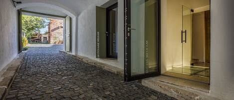 Un pasillo adoquinado que conduce a un acceso con puerta de vidrio y un letrero que dice "UBYTOVANIE WELKAM".