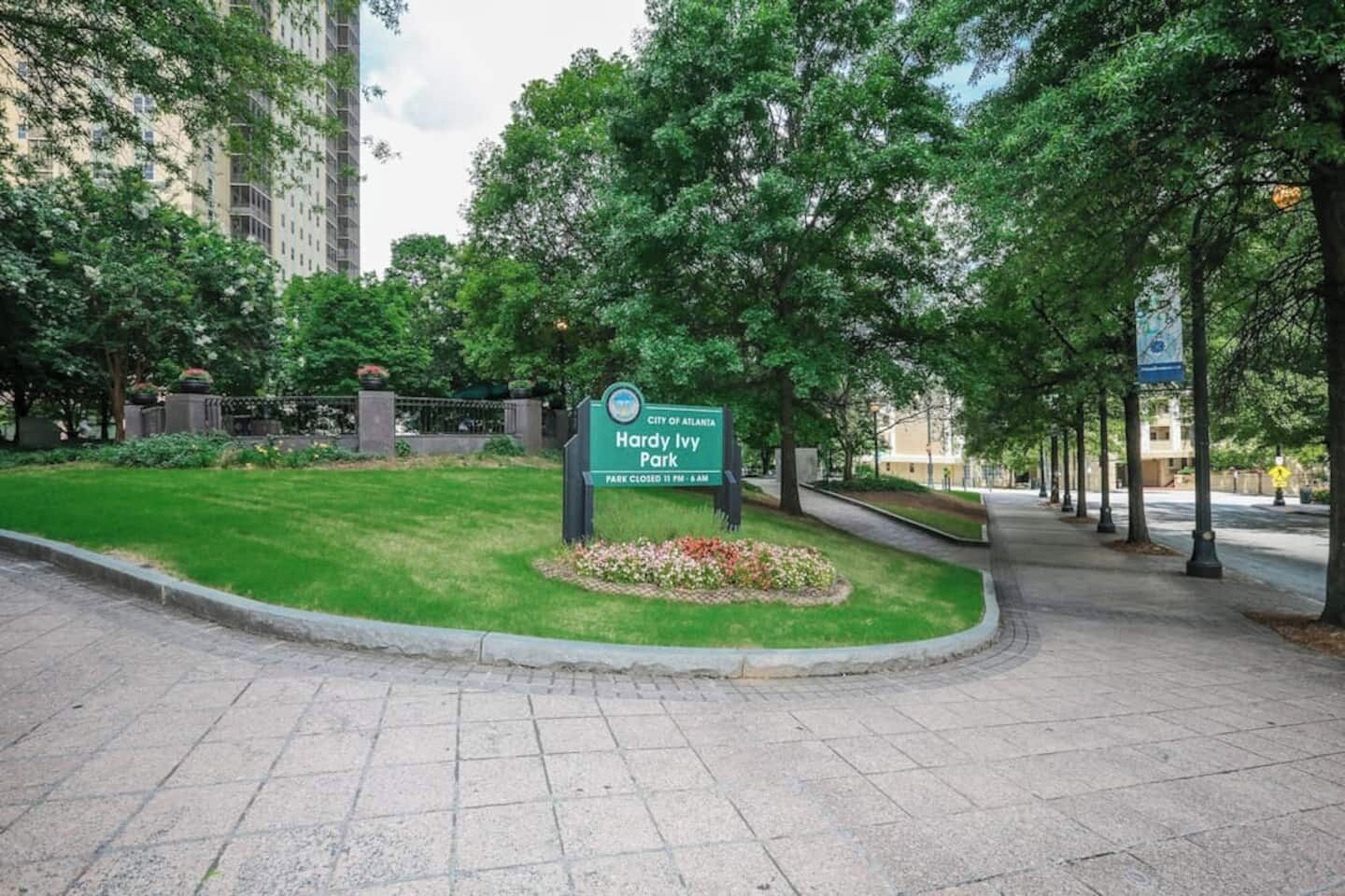 A park entrance sign for Hardy Atlanta Ivy Park with a paved walkway and trees.