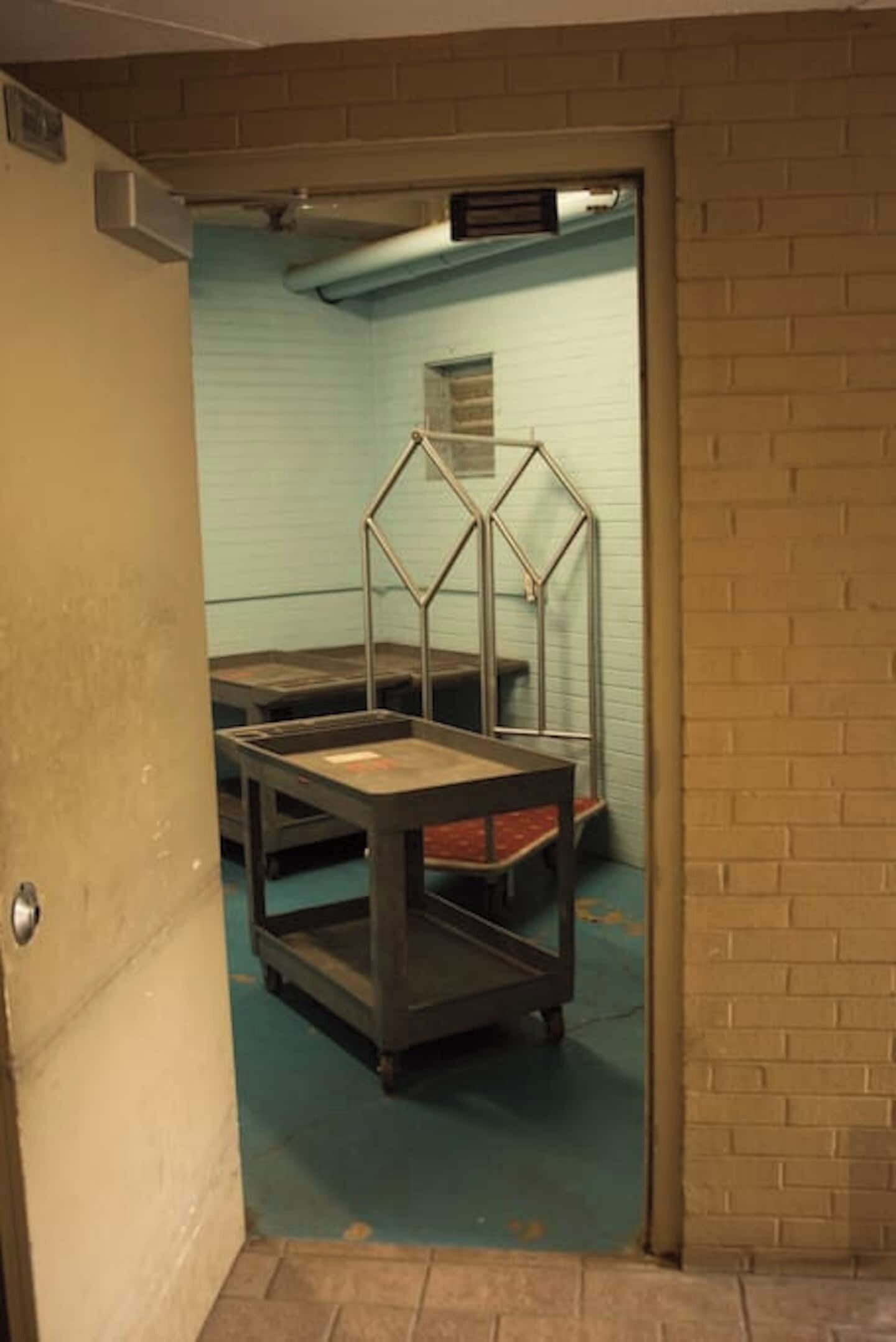 Ein Zimmer mit einem Metalltisch, einer Metallkonstruktion und einer Backsteinwand, sowie einer Tür.