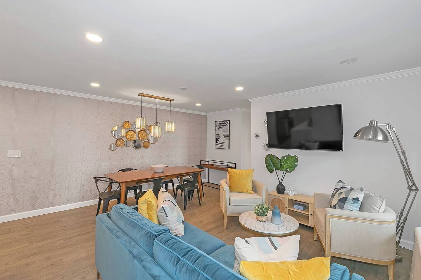 A modern living room with a blue sofa, wooden dining table, and a TV mounted on the wall.