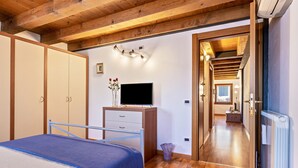 Ein Schlafzimmer mit Bett, Kleiderschrank, Schreibtisch, Fernseher und einem Flur zu einem weiteren Raum.
