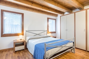 A bedroom with a bed, bedside tables, a wardrobe, and windows.