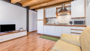 Eine moderne Küche mit weißen Schränken, einer Holzbalkendecke und einem Flachbildfernseher auf einer Holzkonsole.