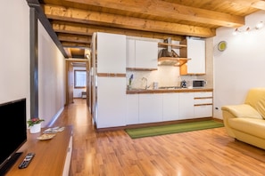 A modern kitchen with wooden beams, white cabinets, a microwave, and a green rug.
