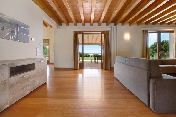 A spacious room with a wooden ceiling, a sofa, a TV, and a view of the outdoors. - 'Villa Sellemond' with Lake View, Pool, Garden & Wi-Fi (Lazise)