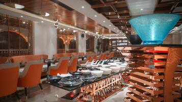 A modern restaurant interior with orange chairs, a central dining table with various dishes, and a unique blue glass bowl on a stand.