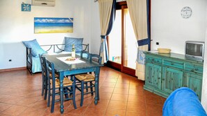 A room with a dining table, chairs, a sofa, a television, and a cabinet. - Awesome apartment in Marinella (SS) with house sea view (Marinella (SS))